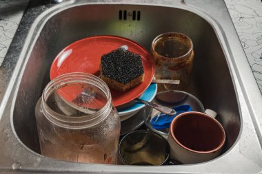 A sink full of dirty dishes. The metal sink is full of dirty plates, mugs and jars. Too lazy to wash dishes