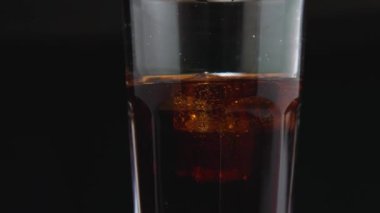 A close-up of a glass with ice cubes and a dark carbonated drink on the kitchen board. The camera flies around. Parallax effect. Ice and bubbles swirl around in the glass
