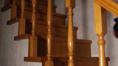 Women's feet in black socks and gray pants climb a wooden staircase. Side view through the balusters. Slow motion. There is a dim light in the house