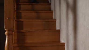 A Caucasian man in jeans, a plaid jacket and black socks descends a wooden staircase. Front view. Evening, a dim light is burning in the house