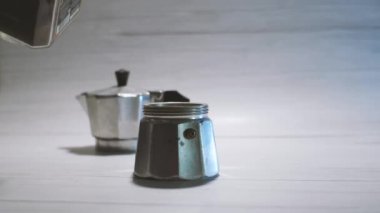 A wooden spoon pours freshly ground coffee into a geyser coffee maker. Light background. The process of making delicious coffee at home