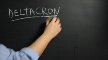 A woman's hand wipes off with a sponge the word Deltacron written in chalk on a black board. Deltacron is a new variant of the coronovirus infection Covid-19
