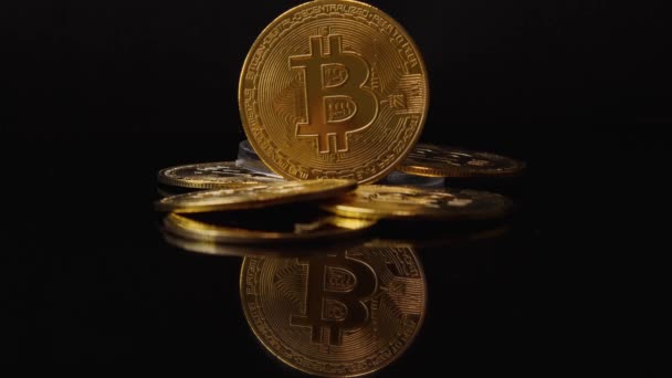 Een gouden cryptogeld Bitcoin munt torens onder een stapel munten. Mooie schittering van licht. BTC munt op zwarte achtergrond met reflectie. — Stockvideo