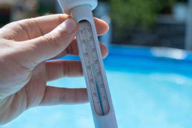 Adamın elinde havuz suyunun sıcaklığını ölçmek için bir termometre var. 30 santigrat derece ya da 85 fahrenhayt. Arka plan mavi sudur.