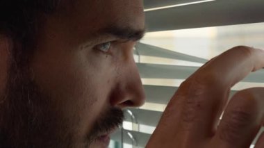 Karanlık bir odada bir adam pencerenin perdelerinden dışarı bakar. Gizli gözetleme. Yakın plan.