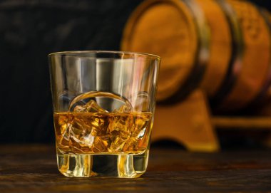 Yarım bardak buzlu viski meşe fıçısının önünde duruyor. Yakın plan.