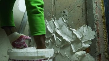 Bir adamın eldivenli eli beton bir duvara malayla alçı sürüyor. Ön planda bir kova alçı var. Ön planda bir kova alçı var. Rusya, Krasnodar, 20 Ekim 2021