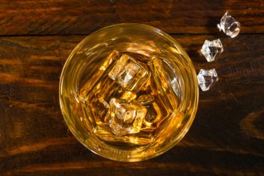 Koyu ahşap bir arka planda buz parçaları ve buzda bir bardak viski var. Üst görünüm, yakın çekim