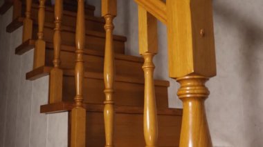 Gri pantolonlu bir kadının çıplak ayakları meşe merdivenlerden iner. Kenardan tırabzanın üstünden bak.