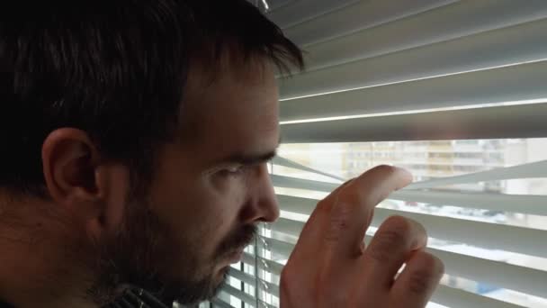 Mężczyzna Brodą Podchodzi Okna Odsuwa Żaluzje Patrzy Przez Pęknięcie Przez — Wideo stockowe