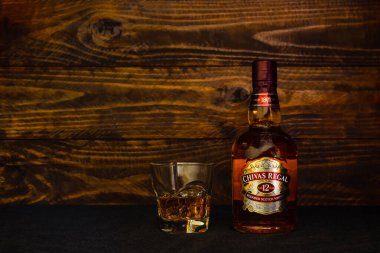 12 yıllık bir şişe Chivas Regal Scotch Whisky ve koyu ahşap arka planda buzlu bir bardak. Karışık İskoç viskilerinin lideri. Rusya, Krasnodar, 11 Aralık 2021