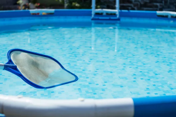 在清澈的水的背景下 从游泳池中清理树叶的叶网 乡间别墅后院里的圆形框架水池和蓝水中的网溜溜者 — 图库照片