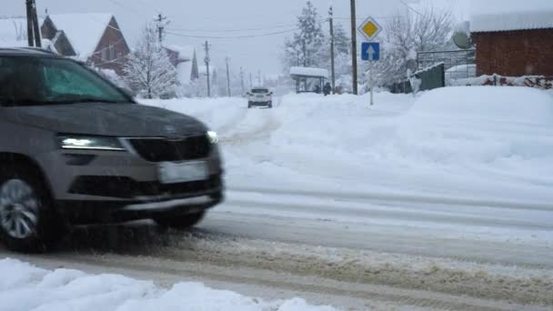 汽车在白雪覆盖的路上行驶 背景是房屋 灰色的冬季天空和降雪 俄罗斯 Goryachiy Klyuch 2022年2月5日 — 图库视频影像