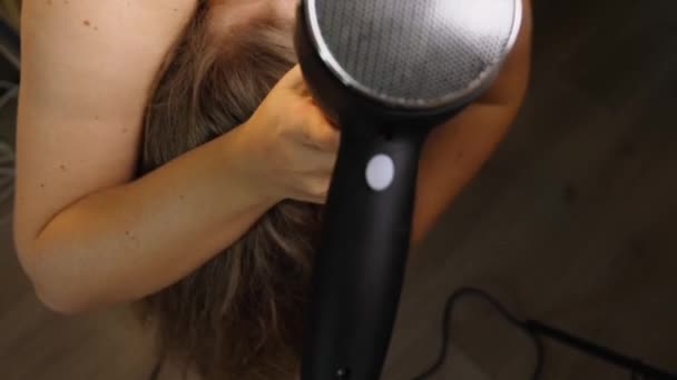 从上方看 一个女人弯下腰 用吹风机擦干她蓬松的头发 特写镜头 有选择的重点 美容美发的概念 — 图库视频影像