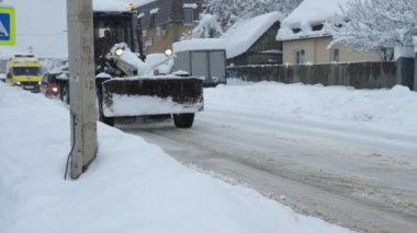 Gradyatör yolu kardan temizler. Arabalar ve ambulanslar onu takip ediyor. Evin arka planında gri bir kış gökyüzü ve kar yağışı vardı. Rusya, Goryachiy Klyuch, 5 Şubat 2022