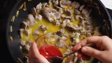 Tavuk Gizzard 'ın içine tavada pişen sebzelerle domates ezmesi döken bir kadının üst görüntüsü. Asya usulü yemek.