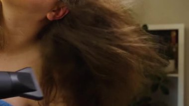 Koyu renk saçlarını saç kurutma makinesiyle kurutan bir kadının yakın çekimi. Kabarık saçlar hava akımından dolayı dalgalanıyor. Seçici odak noktası. Güzellik ve saç bakımı kavramı