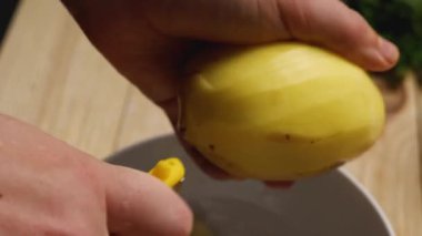 Bir kadının patatesleri soyarken, patates soyma makinesiyle sebzenin derisini yüzerken. Ahşap bir masanın arka planında