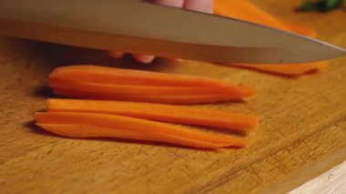 Kesme tahtasındaki keskin bir bıçağın yakın çekimi havuçları pipetlere ayırır. Ağır çekim. Malzemelerin hazırlanması. Her gün sağlıklı ve sağlıklı yiyecekler.