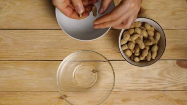 Yukarıdan üç bardak ayakta duran ahşap bir masaya bak. Birinde kabuklarında fıstık var. Bir adamın elleri fıstıkları alıp soyar. Bir kaptaki deriler ve diğerindeki fıstıklar.