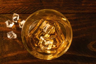 Yanında buz küpleri olan buzlu bir bardak viskinin üstünden bak. Koyu tahta arkaplan