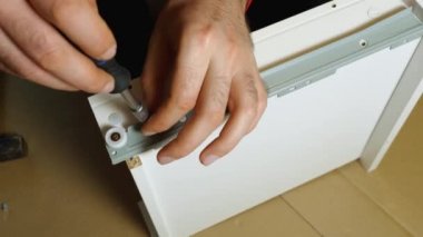 Bir adamın ellerinin bir tornavidayı raf korkuluğuna vidaladığı yakın plan. Üst Manzara. Evde kendi elleriyle mobilya montajı yapıyor..