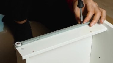 Bir adamın ellerinin bir tornavidayı raf korkuluğuna vidaladığı yakın plan. Evde kendi elleriyle mobilya montajı yapıyor..