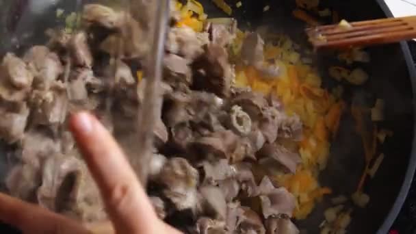 Bovenaanzicht van een vrouwenhand in een wok met gebakken uien en wortelen gegoten Chicken Gizzard en geroerd met een houten spatel. Een close-up. Koken in Aziatische stijl. — Stockvideo