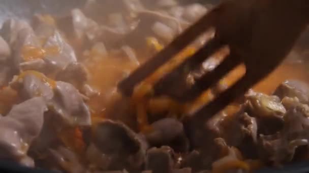 In slow motion, een houten spatel roert de kip bijproducten in de wok. Er komt stoom uit de schotel. Een close-up. Koken in Aziatische stijl. — Stockvideo