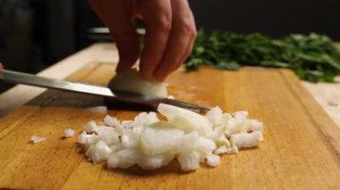 Kesme tahtasının üzerinde soğan doğrayan bir bıçakla yakın çekim. Maydanoz arka planda yatıyor. Seçici arka plan. Malzemelerin hazırlanması. Her gün sağlıklı ve sağlıklı yiyecekler..