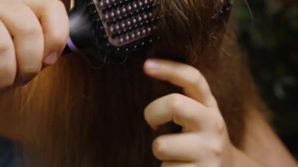 Κοντινό πλάνο ενός κοριτσιού που βουρτσίζει και στεγνώνει τα μαλλιά της με ένα ηλεκτρικό ίσιωμα μαλλιών. Θερμαινόμενη, κεραμική, μη καταστρεπτική βούρτσα μαλλιών. Φροντίδα μαλλιών. — Αρχείο Βίντεο