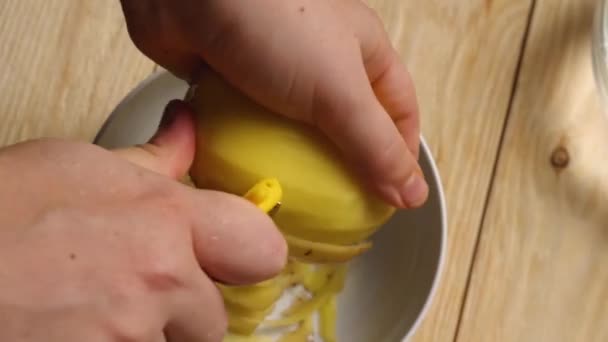 Close-up van een vrouw handen over een kom aardappelen schillen met een gele aardappelschiller. — Stockvideo