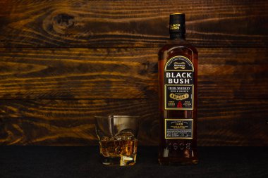 Bir şişe Bushmills Black Bush İrlanda viskisi ve koyu ahşap arka planda buzlu bir bardak. Dünyanın en iyi ve en iyi İrlanda viskilerinden biri. Rusya, Krasnodar, 11 Aralık 2021