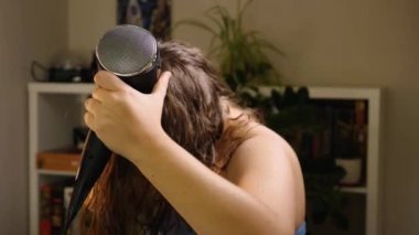 Beyaz bir kadın oturma odasında dururken saçını saç kurutma makinesiyle kurutur ve tarar. Seçici Odaklanma. Güzellik ve saç bakımı kavramı