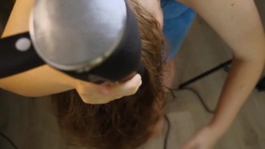 Koyu renk saçlarını kurutma makinesiyle kurutmak için eğilmiş bir kadının yakın çekimi. Üst görünüm, seçici odaklanma. Güzellik ve saç bakımı kavramı