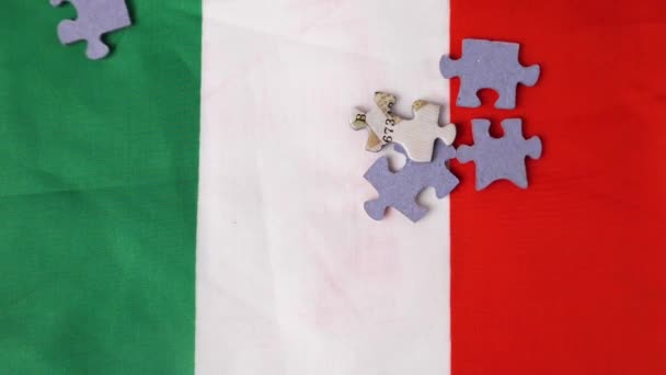 スローモーションでは カラフルなジグソーパズルのピースがイタリアの国旗に落ちます イタリアのパズルメーカーの概念 — ストック動画