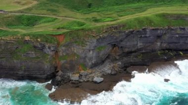 Dalgalı bir denizin üzerindeki yeşil doğal alandaki kayalık bir sahil uçurumunun havadan görünüşü. Ada, Cantabria, İspanya. 4K
