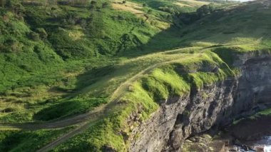 Dalgalı bir denizin üzerindeki yeşil doğal alandaki kayalık bir sahil uçurumunun havadan görünüşü. Ada, Cantabria, İspanya. 4K