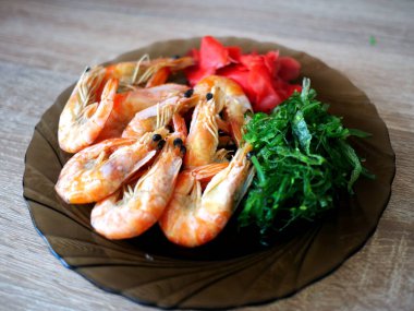 Büyük kral karidesler siyah bir tabakta yatar, ahşap masa yemek için güzel bir zemin. Restoran ya da mağaza reklamı için boş yer var. Taze deniz yemeği teslimatı. Pahalı.