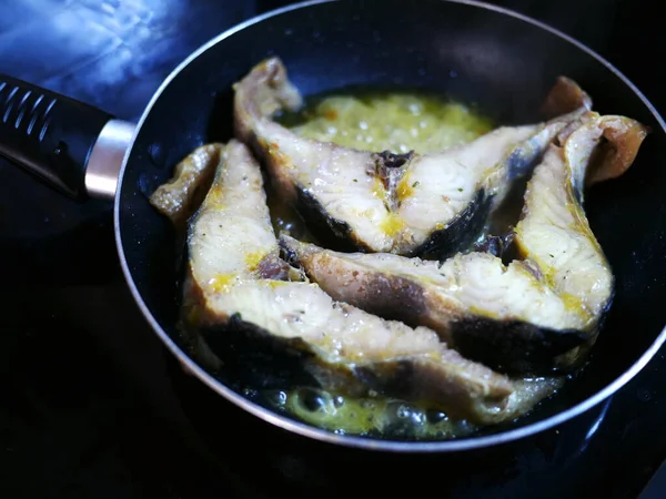 Three slices of cut fish are fried in sunflower oil in a black frying pan. Delicious food for an elite restaurant. Round frying pan without lid. Horizontal banner for advertising a cookbook or blog