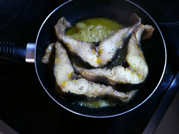 Three slices of cut fish are fried in sunflower oil in a black frying pan. Delicious food for an elite restaurant. Round frying pan without lid. Horizontal banner for advertising a cookbook or blog