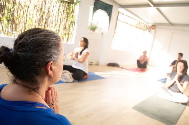 Orta yaşlı yoga öğretmeni, kendisiyle aynı hareketleri yapan öğrencilerini denetlerken minderinde dua ediyor..