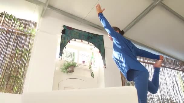 这位身穿蓝色衣服的瑜伽老师一边做伸展运动 一边看她的笔记本电脑 一边在家里给她的学生们上网络课 — 图库视频影像
