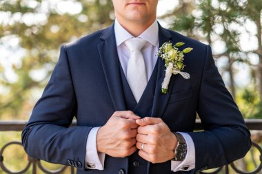 Zarif koyu mavi takım elbiseli, güzel beyaz gül yaka çiçekli, tanınmaz bir genç damat. Damat moda çekimi.