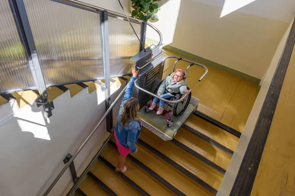 電動車椅子リフトを使用して公共の建物にアクセスするために脳性麻痺に住んでいる幼い子供を持つ母親 車椅子ユーザーのための特別なリフトプラットフォーム 障害者用階段リフト設備 — ストック写真