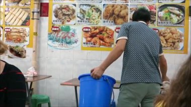 Hong Kong, Asya - 20 Kasım 2019: Meşgul Kowloon Temple Street market restoranında masaları temizleyen adam. Adam meşgul restoranda masaları plastik kovaya boşaltıyor.