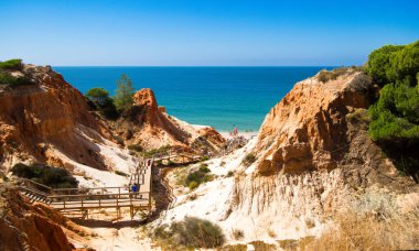 Turistlerin Portekiz 'in Algarve kentindeki Falesia' da bir yaya köprüsünde mavi denizde sona eren turuncu kayalıklar.