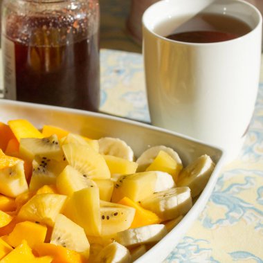 Kahvaltı için büyük bir tabak egzotik meyve, mango, muz, çay ve çilek reçelli bir masada altın kivi.