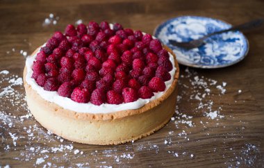 Ahududulu kek ve ahşap bir masada mavi porselen tabak.