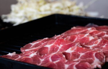 Barbekü yapmak için, domuz eti ince, dairesel tabaklara kesilir ve siyah tepsiye konur..